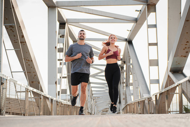 Young couple running for health, wellness or training for a marathon, competition or race, showing effort and endurance enjoying the cardio sport. Workout of a fitness man and athletic woman jogging - Photo, Image