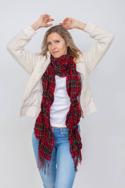 Mooie volwassen vrouw in een warme rode sjaal poseren tegen een grijze achtergrond. - Foto, afbeelding