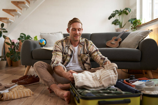 Portrait of man with suitcase, thinking what to bring on holiday, preparing for vacation, packing luggage. - Photo, Image