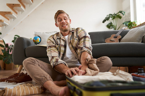 Портрет мужчины, который пытается уместить одежду в полный чемодан, упаковывая багаж для отдыха или деловой поездки. - Фото, изображение