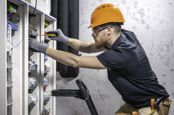 un electricista macho trabaja en una centralita con un cable de conexión eléctrico
. - Foto, imagen