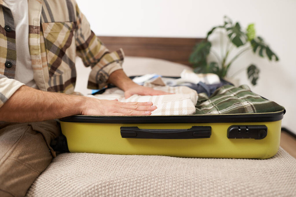 Colpo ritagliato di mani maschili che mettono i vestiti dentro la valigia, fanno i bagagli per il viaggio di lavoro o andare in vacanza, si preparano per il viaggio di vacanza, preparano i bagagli. - Foto, immagini