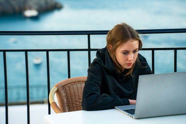 Genç bir kız gün batımında balkonda dizüstü bilgisayar kullanıyor.. - Fotoğraf, Görsel