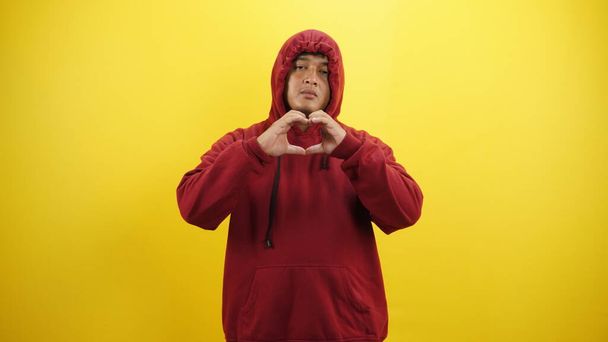 Junge kaukasische Mann macht eine Herzform auf einem roten isolierten - Foto, Bild
