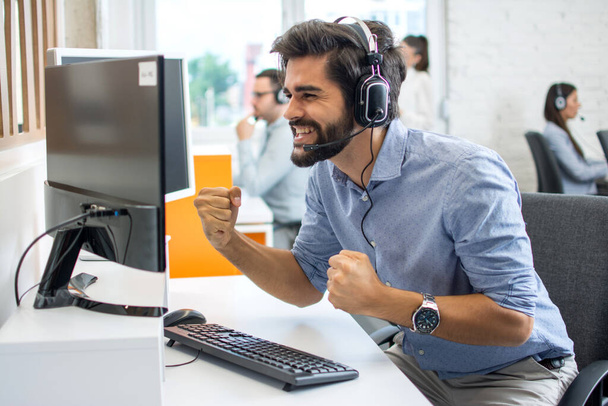 Euforyczny pracownik telefoniczny z słuchawkami świętującymi dobrą pracę w miejscu pracy. - Zdjęcie, obraz