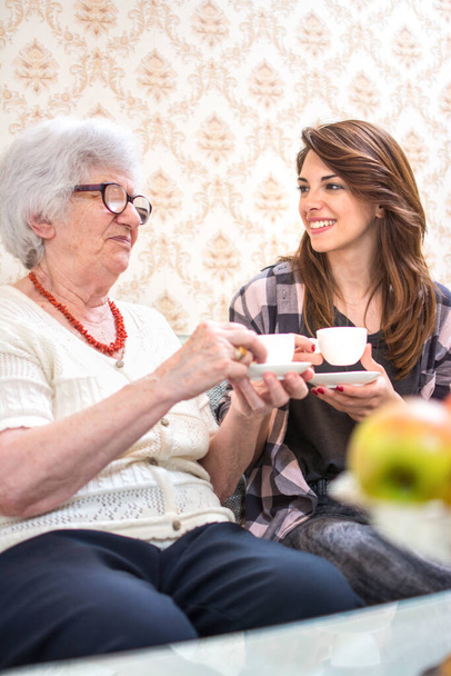 Großmutter und Enkelin sitzen zusammen am Tisch, reden und trinken Kaffee. - Foto, Bild