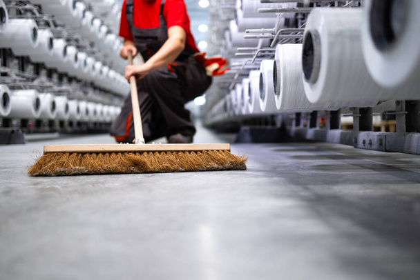 Αγνώριστο πάτωμα καθαρισμού εργαζομένων με σκούπα. Διατήρηση του εργοστασίου τακτοποιημένο και καθαρό. - Φωτογραφία, εικόνα