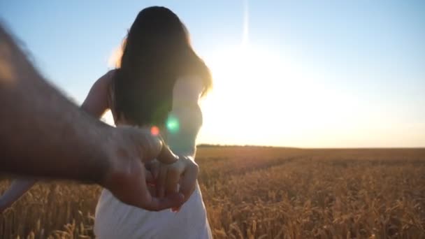 Kobieta trzymająca męską rękę i biegnąca przez niekończące się pole pszenicy. Młoda para korzystająca z wolności i wypoczynku na świeżym powietrzu w środowisku wiejskim. Piękny jasny zachód słońca w tle. POV Zwolniony ruch. - Materiał filmowy, wideo