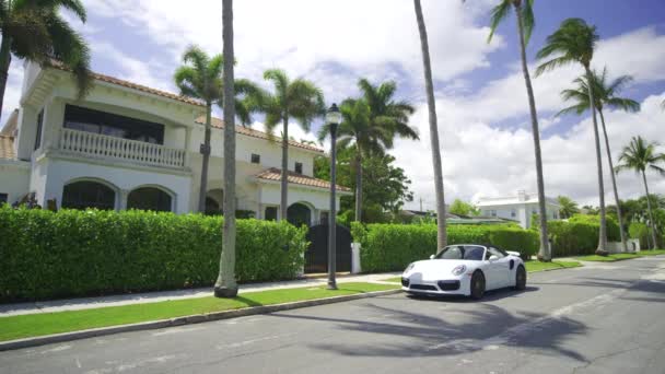 West Palm Beach, FL, USA - 2024. március 24: Luxus West Palm Beach-i villa fehér Porsche Turbo-val kint parkol - Felvétel, videó
