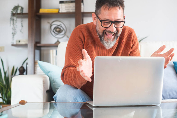 Dospělý běloch nosí brýle sedět na pohovce doma mluvit o videohovoru na notebooku, na volné noze muž pracující on-line mají webovou kameru virtuální on-line konferenční konverzace na počítači s klientem vzdálený - Fotografie, Obrázek