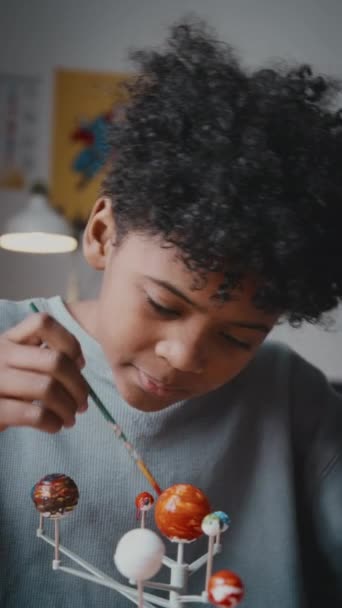 Függőleges portré lövés vidám kis afro-amerikai fiú színező barkácsoló naprendszer festékkel és mosolyog a kamera, miközben csinál kézműves otthon - Felvétel, videó