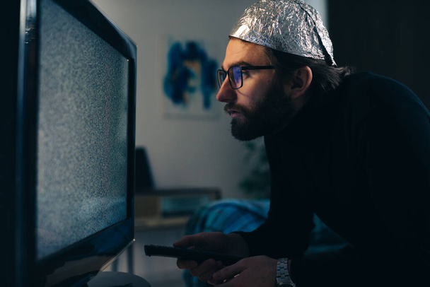 Muž v plechové fólie klobouk a přikrývka sledování TV interference - Fotografie, Obrázek