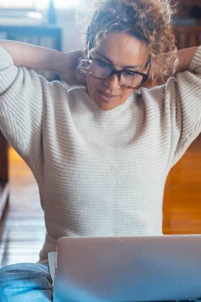  woman stretching her shoulder and arms after finishing to work at home on laptop sitting on the floor. Indoor leisure activity. People and computer connection. Remote working. Small business lady - Photo, Image