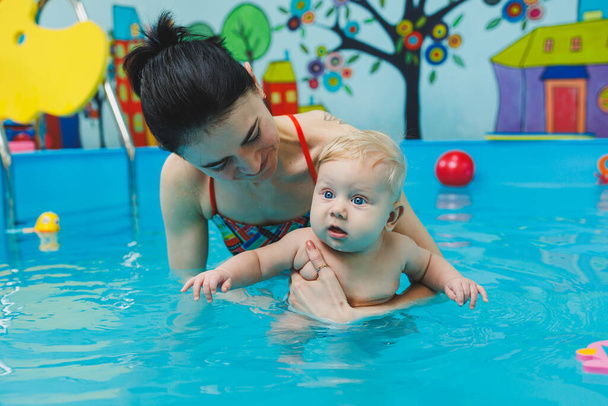 Kuusikuukautinen vauva oppii uimaan valmentajan kanssa altaassa. Uima-allas vauvoille. Lasten kehitys - Valokuva, kuva