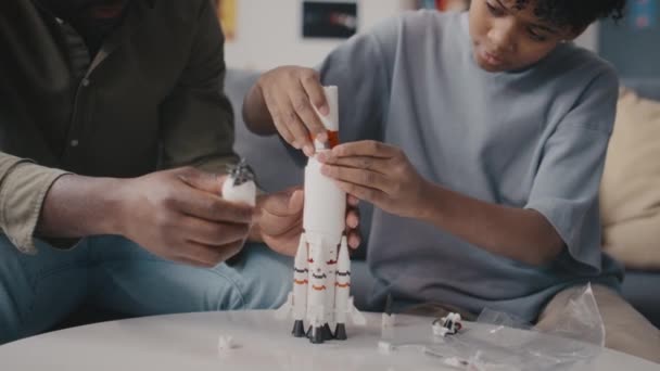 Kleiner afroamerikanischer Junge baut mit Hilfe seines Vaters Raketenmodell, während er den Tag zu Hause verbringt - Filmmaterial, Video