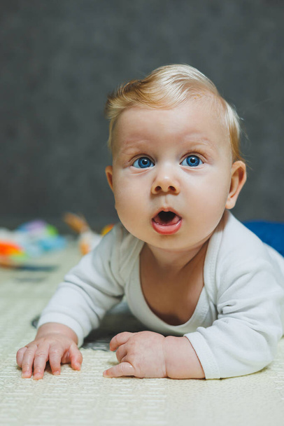 Un bambino di quattro mesi giace sul pavimento su un tappeto e gioca con i giocattoli. Il bambino tiene la testa. Un bambino impara a strisciare sul pavimento - Foto, immagini