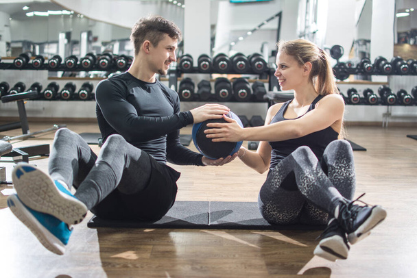 Αθλητικό ζευγάρι γυμναστικής κάνει κοιλιακές ασκήσεις με μπάλα φάρμακο στο γυμναστήριο. - Φωτογραφία, εικόνα