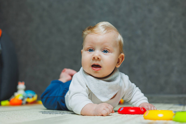 Ein süßer fünf Monate alter Junge liegt und spielt auf einem Teppich. Kind auf dem Boden. Ein süßes kleines Baby lernt zu krabbeln. - Foto, Bild
