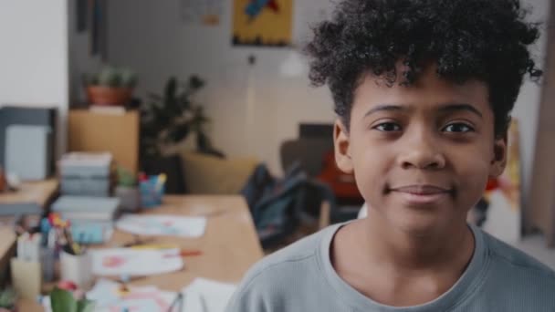 Portret małego Afroamerykanina z kręconymi włosami stojącego w domu i pozującego do aparatu z uśmiechem - Materiał filmowy, wideo