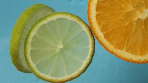Levendige plakjes sinaasappel en limoenschar zachtjes op het wateroppervlak, citrusschijfjes creëren pittoreske taferelen terwijl ze prachtig zweven met rustig blauw water Kijk toe hoe sinaasappel en limoenschijfjes serenel drijven - Video