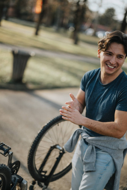Веселий молодий дорослий відпочиває поруч зі своїм велосипедом в сонячному парку, виключаючи щастя і активний спосіб життя. - Фото, зображення