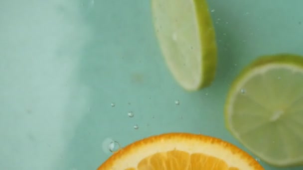 Fényes narancs- és lime szeletek lustán táncolnak a víz felett, ahogy a citrusszeletek lebegnek, a narancs- és lime szeletek mozgása, ahogy kecsesen navigálnak a szelíd áramlatokban Egészséges táplálkozási fogalom - Felvétel, videó