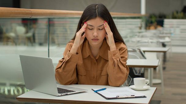 Stressed tired Asian woman working in cafe with laptop paperwork problem business difficulty sick unhealthy chinese korean businesswoman has painful head headache migraine suffer hurt tension overwork - Photo, Image