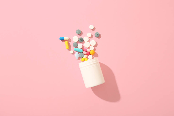 Tarro con diferentes píldoras sobre fondo rosa - Foto, Imagen