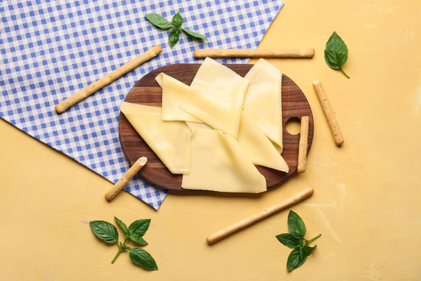 Deska s chutnými plátky sýra, listů bazalky a italských Grissini na béžovém pozadí - Fotografie, Obrázek