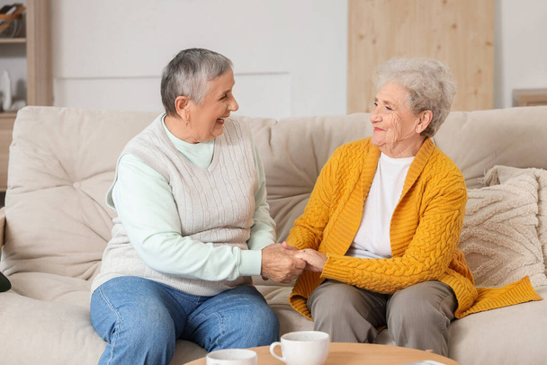 Idősebb női barátok fogják egymás kezét a kanapén otthon - Fotó, kép
