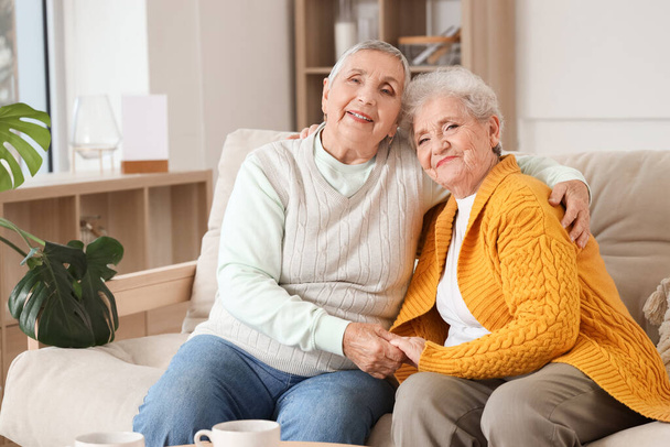 Senior vrouwelijke vrienden knuffelen op de bank thuis - Foto, afbeelding