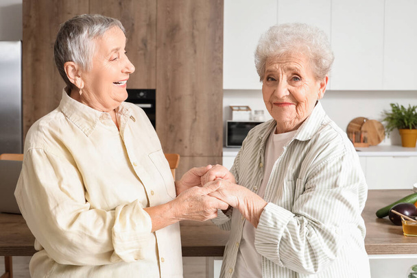 Senior female friends holding hands in kitchen - Photo, Image