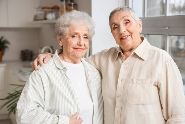 Старшие подруги обнимаются на кухне - Фото, изображение