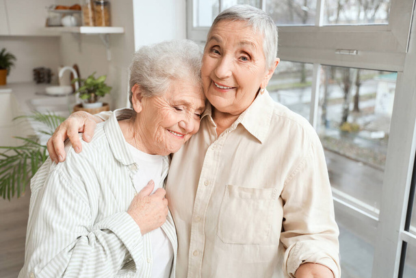 Senior female friends hugging in kitchen - Foto, imagen