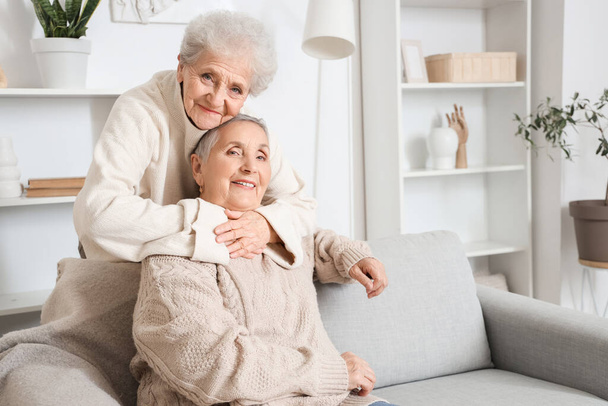 Senior woman hugging her friend on sofa at home - Fotó, kép