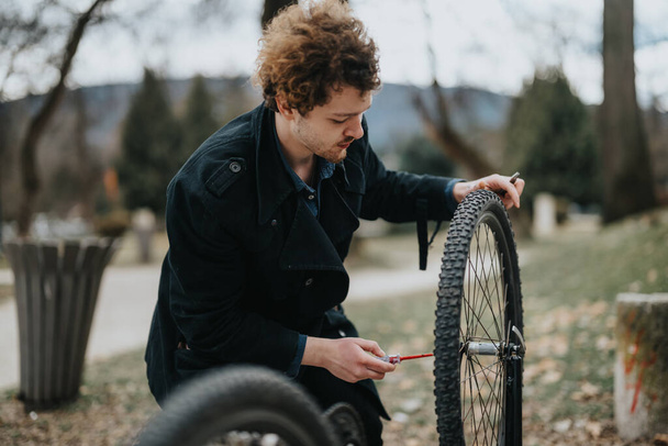 Um jovem empresário repara sua bicicleta no parque, mostrando habilidades de resolução de problemas e autossuficiência. - Foto, Imagem