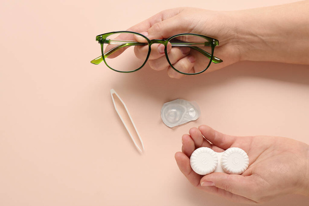 Γυναικείο χέρι με γυαλιά, δοχείο για φακούς επαφής και τσιμπίδα σε μπεζ φόντο - Φωτογραφία, εικόνα