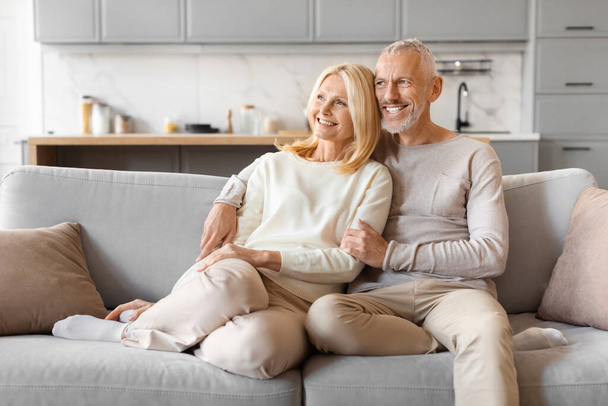 Liebevolles Seniorenpaar sitzt gemütlich auf einer Couch und vermittelt Zufriedenheit und Kameradschaft - Foto, Bild