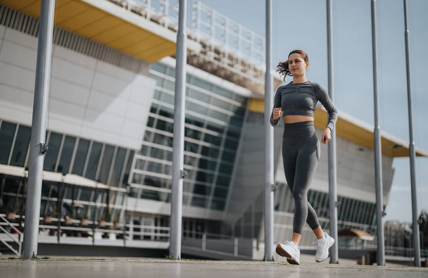 Aktywna młoda kobieta w sportowym bieganiu w nowoczesnym środowisku miejskim, prezentująca zdrowy styl życia i determinację. - Zdjęcie, obraz