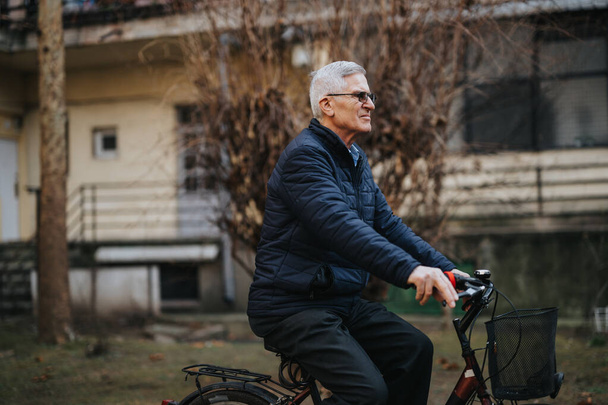 Старший чоловік з сірим волоссям насолоджується їздою на велосипеді, сприяючи здоровому і активному способу життя в тихому передмісті. - Фото, зображення