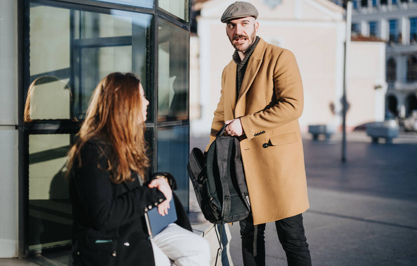 Stílusos férfi kabátban tartja hátizsák beszél ülő nő a városban. - Fotó, kép