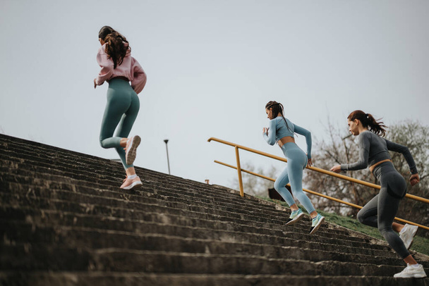 Arkadaşlarla dışarıda antrenman yapmak, spor kıyafetleri içinde üç kadının basamakları tırmanarak aktif bir yaşam tarzını resmetmek.. - Fotoğraf, Görsel