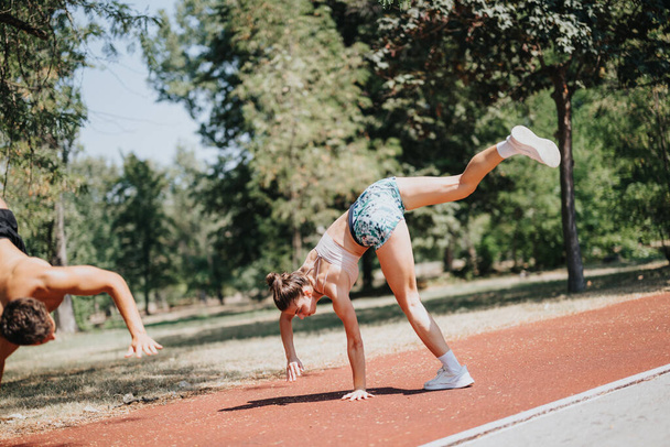 Fit sportspeople, a man and woman in sportswear, doing cartwheels. They inspire with their athleticism and outdoor workout in a sunny park. Training and positive results lead to better body shape. - Photo, Image