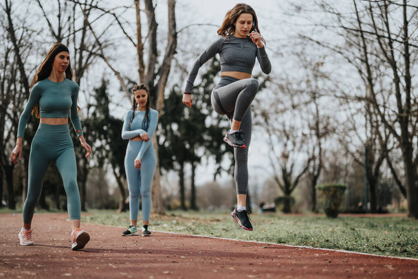 Three athletic women in matching workout gear doing exercises on a track in a tranquil park setting. - Photo, Image