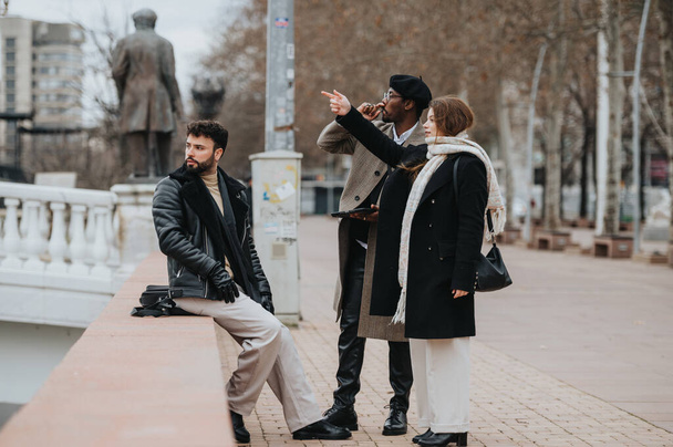 Tres jóvenes emprendedores discuten el trabajo mientras están de pie en un parque de la ciudad con tabletas y computadoras portátiles, mostrando flexibilidad de trabajo remoto. - Foto, Imagen