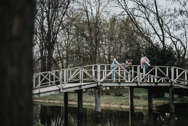 Trois femmes en vêtements de sport se livrent à une routine d'étirement sur un pont extérieur, fixant des objectifs de remise en forme au milieu d'une nature tranquille. - Photo, image