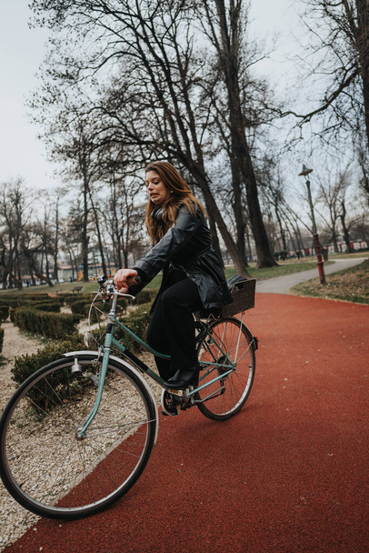Молодая и привлекательная деловая женщина, наслаждающаяся велосипедной прогулкой в парке, демонстрирующая стиль и уверенность - Фото, изображение
