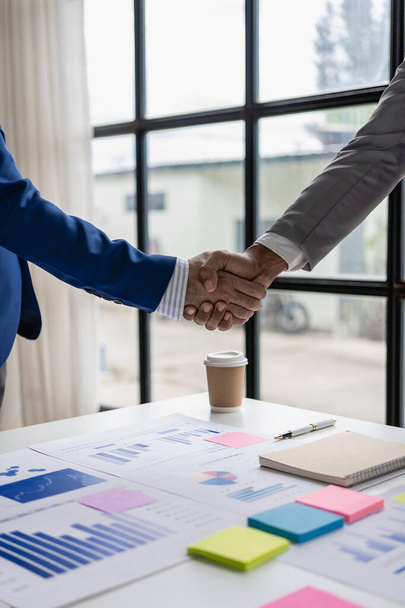 Businessman and investor holding hands as a symbol of friendship and cooperation in business success of cooperation and with documents, financial graphs and laptop on the table. Close-up photo. - Photo, Image