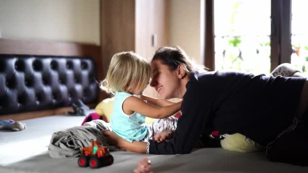 Mamá juega con su hijita, la abraza, le besa la barriga mientras está sentada en la cama. Imágenes de alta calidad 4k - Imágenes, Vídeo