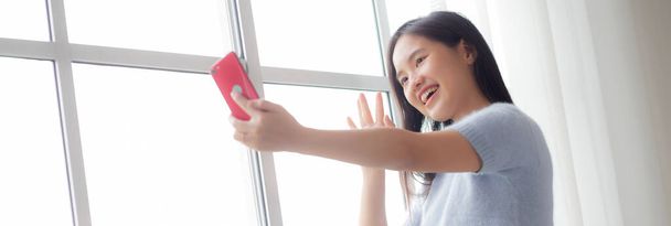 Felicidad joven mujer asiática videollamada con teléfono inteligente en la sala de estar en casa, mujer sonriendo y utilizando las redes sociales en línea con el teléfono inteligente en casa, estilos de vida y concepto de comunicación. - Foto, imagen